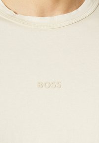 Krémové bavlněné tričko s kulatým výstřihem a jemně vylisovaným logem "BOSS" na přední straně. Hladká textura a přiléhavý střih.