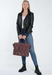 Quiltet bordaux-læder tote taske med to håndtag, lynlås-lukning og geometrisk mønster. Båret med en sort læderjakke og blå jeans.