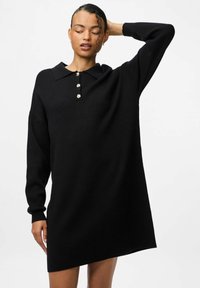 Melnas džemperkleitas ar apkakles izgriezumu, trim dekoratīviem pogām, garām piedurknēm un asimetrisku apakšmalu. Izgatavota no mīkstas, teksturētas auduma.