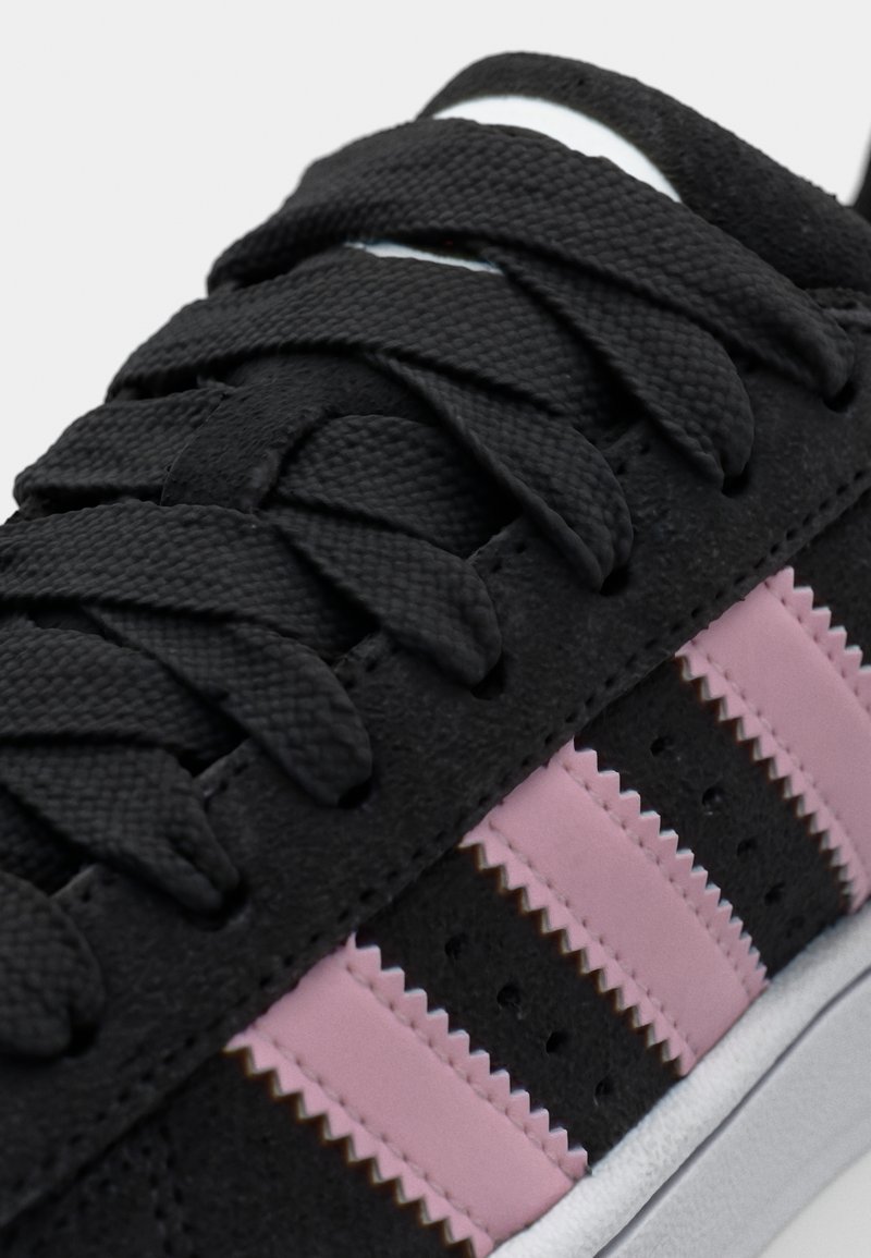 Sneaker in suede nero con design a tre strisce rosa, lacci testurizzati e suola bianca. Presenta dettagli perforati e cuciture a zigzag.