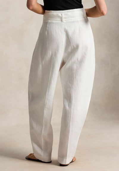 Λευκό παντελόνι από λινό, με ψηλή μέση και φαρδιά μπατζάκια, φορεμένο από άτομο που στέκεται ξυπόλυτο σε ουδέτερο φόντο, με μαύρο τοπ μερικώς ορατό.