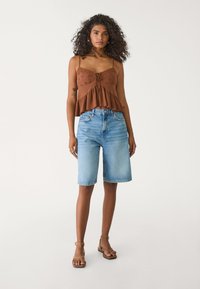 Brun, texturerad ärmlös topp med en knytning framtill; ljusblå denimbermuda-shorts; bruna sandaler.