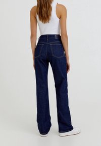 Jeans de tiro alto azul oscuro con piernas anchas, que presentan costuras contrastantes, dos bolsillos traseros y un detalle de cinturilla suave.
