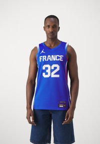 Maglia da basket blu con "FRANCE" e numero "32" in bianco. Presenta il logo Jordan, design senza maniche e sfumatura di colore.