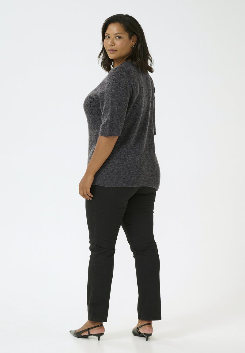 Ciemnoszara sweter z dzianiny z krótkimi rękawami, połączony z czarnymi spodniami slim-fit i czarnymi butami na obcasie. Gładkie tło.