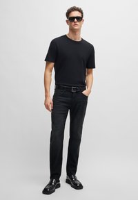 Schwarzes Baumwoll-T-Shirt, dunkle Jeans, schwarze Lederschuhe und Sonnenbrille. Schlichtes Design mit einer taillierten Silhouette und minimalen Details.