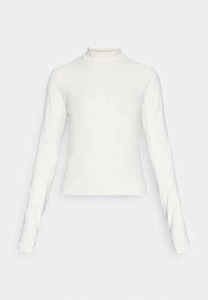 Hosszú ujjú fehér sportfelső, mokk nyakkal és kis középre helyezett logóval a mellkasán, egyszerű háttér előtt.