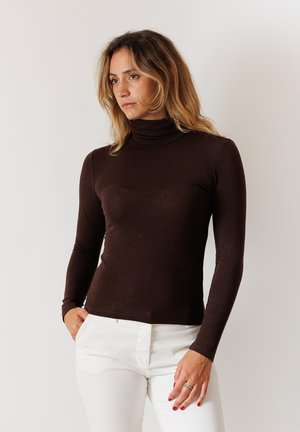 Maglione a collo alto marrone con maniche lunghe, design aderente, texture morbida e leggera lucentezza, abbinato a pantaloni bianchi.