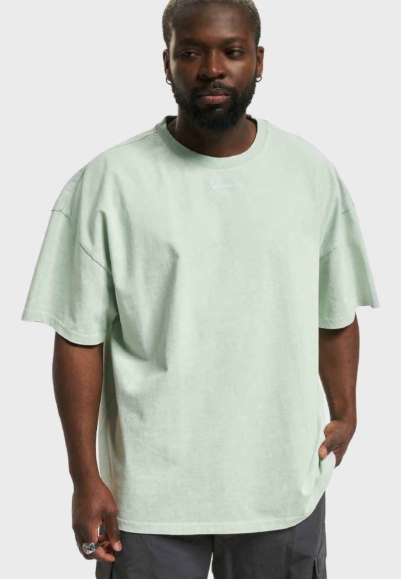 Tricou supradimensionat de culoare verde deschis, cu guler rotund, mâneci scurte și detalii subtile cu logo pe piept. Fabricat dintr-un material moale, cu o croială lejeră.