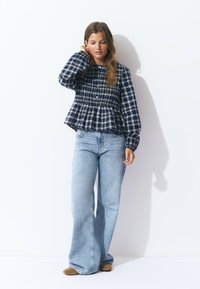 Navy and white checkered peplum blouse with button front, loose sleeves, paired with light blue wide-leg jeans and tan slip-on shoes.