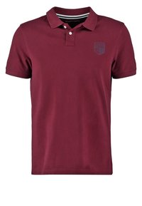 Polo shirt bordeaux en coton, doté d'un col classique, de manches courtes et d'un discret emblème sur la poitrine. Texture lisse et design ajusté.