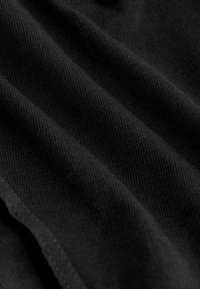 Musta kangas, jossa on poimuttuva kuviointi, pehmeät ja sileät linjat sekä hieman kiiltävä pinta. Materiaali näyttää kevyeltä ja joustavalta.