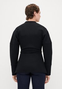 Svart langermet topp laget av et mykt stoff, med en tettsittende midje og belte, samt en lett utsvingt kant. Ingen synlige mønstre eller detaljer.