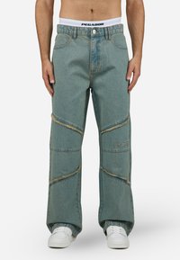 Lichtblauwe denim broek met een relaxed fit, voorzien van rafelige diagonale accenten en geborduurd logo. Gestyled met een witte tailleband.