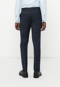 Slim-fit marinblå kostymbyxor i ett slätt tyg, med två bakfickor och en platt frontdesign, kombinerat med svarta läderskor.