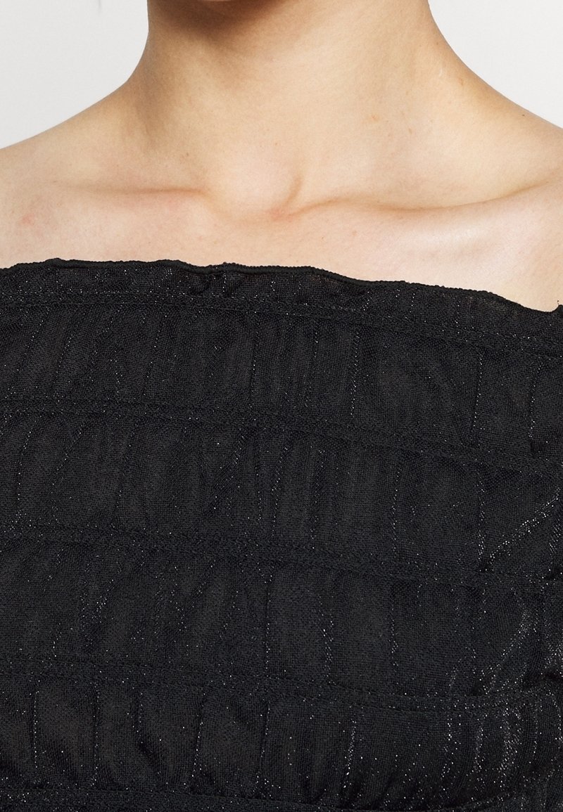 Svart tygtop med en texturerad, rynkad design, med horisontella ränder och en subtil glans. Axelbandslös med en rak halsringning.