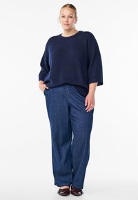 Suéter de punto azul marino con cuello redondo y corte holgado, combinado con pantalones de mezclilla de pernera ancha que cuentan con una cintura ajustable.