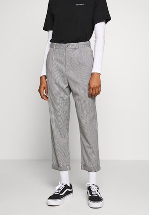 Person wearing grey checkered tapered pants, white socks, black sneakers, black Carhartt T-shirt over a white long-sleeve shirt.