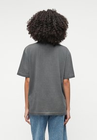 Šedé bavlnené tričko s voľným strihom, krátkymi rukávmi a okrúhlym výstrihom. Obsahuje viditeľné švy a jemne rozstrapkaný lem.