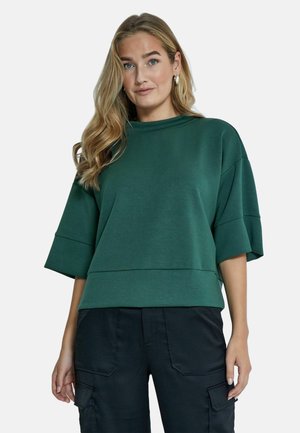 Zeleni oversized dukserica s visokim ovratnikom, širokim rukavima i lagano skraćenim rubom. Izrađena od mekanog, teksturiranog materijala.