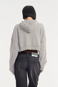 Lühendatud hall kapuutsiga sviiter, ribaga äär ehk pits, ja lahtine lõige, kombineeritud tumedate triibuliste teksadega, mille vööl on nähtav "RAGGED" silt.