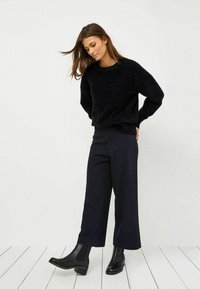 Maglione nero in pelliccia sintetica con vestibilità ampia, abbinato a pantaloni neri a gamba larga e stivaletti con tacco basso a blocco. Design semplice e moderno.