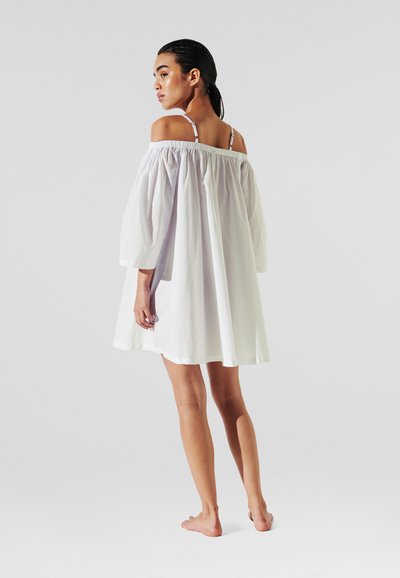 Robe blanche à épaules dénudées, avec des manches bouffantes, de longueur genou, fabriquée en tissu léger, avec des bretelles ajustables et une coupe décontractée.