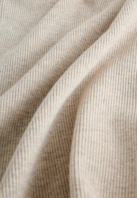 Tessuto beige testurizzato con righe verticali e sottili macchie marroni, che mostrano morbidi pieghe e un aspetto leggero e soffice.