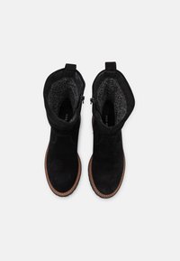 Botas de tobillo de ante negras con un forro texturizado gris, punta redonda, suela marrón cosida y dos lengüetas para facilitar el uso.