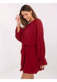 Czerwona sukienka z szyfonu z długimi rękawami, falbanką z przodu i elastycznym paskiem w talii. Luźny krój z lekkiego, zwiewnego materiału.