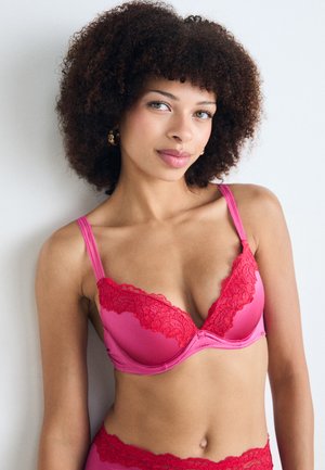 Rosa BH mit Spitzenbesatz und tiefem Ausschnitt sowie verstellbaren Trägern. Glattes Material in lebendiger Farbe, mit floralem Spitzenakzent.