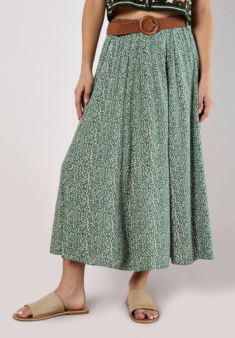 Green, pattern-printed maxi skirt with white spots, featuring a textured brown belt and pleated design. Paired with beige slide sandals.