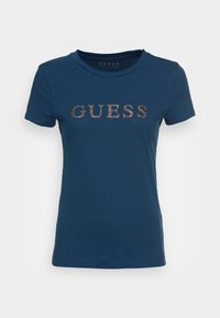 Mörkblå kortärmad t-shirt med rund halsringning, med "GUESS" logotyp i glittrande guldbrev över bröstet.