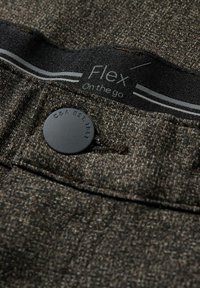 Pánské tmavě hnědé texturované kalhoty s černou značkou na pásu s nápisem "Flex On the go" a černým knoflíkovým zapínáním s logem značky.