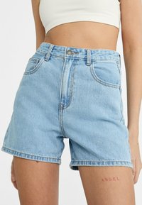 Pantalones cortos de mezclilla azul claro con una cintura alta, cinco bolsillos y un dobladillo deshilachado. La tela presenta una textura sutil con costuras visibles.