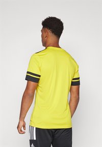 Yellow athletic t-shirt with short sleeves, black stripes on sleeves, lightweight fabric, and a crew neckline, worn with dark athletic shorts.