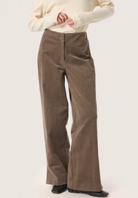 Brown corduroy wide-leg trousers with a high waist and textured fabric, paired with a light-colored long-sleeve top.