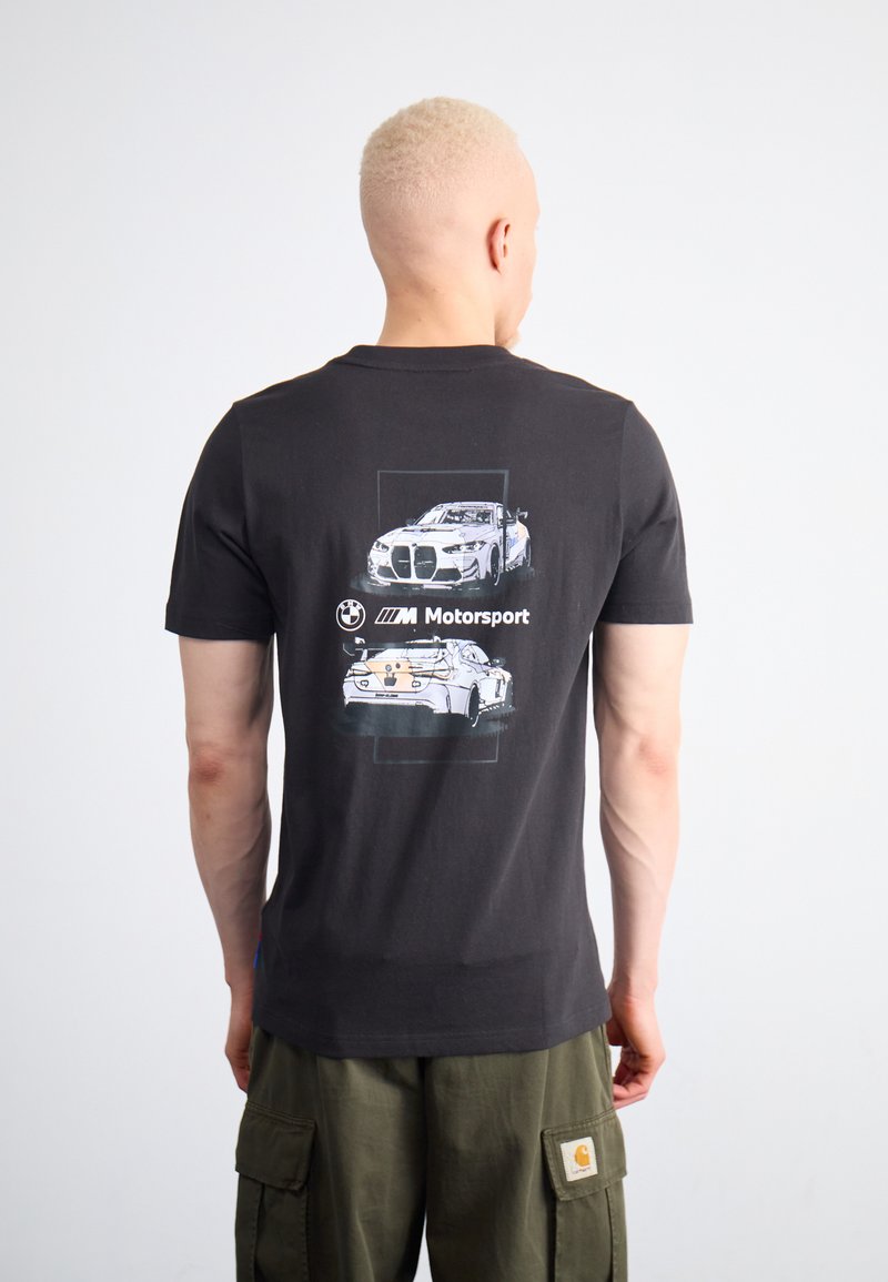 Camiseta negra con un gráfico de coches de motorsport de BMW en la parte trasera. Mangas cortas, cuello redondo, hecha de algodón. Diseño simple y moderno.
