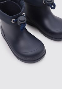 Stivali in gomma waterproof di colore blu navy con punta arrotondata, caratterizzati da una texture liscia e dettagli decorativi in corda blu navy nella parte superiore.