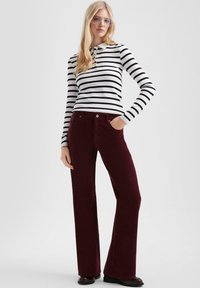 Zwart-wit gestreepte lange mouwen polo shirt gecombineerd met bordeauxrode corduroy flared broeken. Opvallende details zijn onder andere knoopaccenten en zakken.
