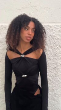 Zwarte jurk met lange mouwen, gedraaide taille en zilverkleurige accenten. Voorzien van een open detail en een gladde, licht gestructureerde stof.