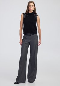 Czarny bezrękawnik z golfem ozdobiony detalami na ramionach, w połączeniu z szarymi spodniami z wysokim stanem i plisami oraz czarnym obuwiem.