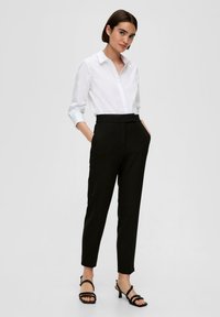 Camicia bianca con colletto, abbinata a pantaloni neri a vita alta e sandali neri con tacco a strappo. Tessuto morbido, taglio su misura.