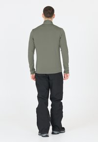 Langærmet, olivengrøn bluse lavet af let stof, parret med sorte bukser. Enkel design med høj krave og tætsiddende silhuet.