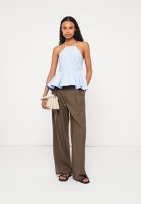 Svetlomodrý peplum top s halter krkom, skombinovaný s hnedými širokými nohavicami s vysokým pásom a čiernymi sandálmi. Minimalistická béžová kabelka.