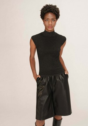 Haut noir sans manches avec un col haut, fabriqué en tissu texturé ; associé à un short en cuir noir ample. Une légère brillance est visible.