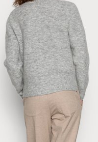 Szary sweter dzianinowy o strukturalnym wykończeniu, z luźnym krojem i ściągaczami na rękawach, w zestawieniu z beżowymi spodniami z tylnymi kieszeniami.
