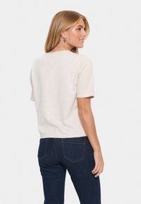 Lichtbeige kortemouwen sweater met een losse pasvorm en geribbeld textuur, gecombineerd met donkerblauwe jeans met standaard achterzakken.