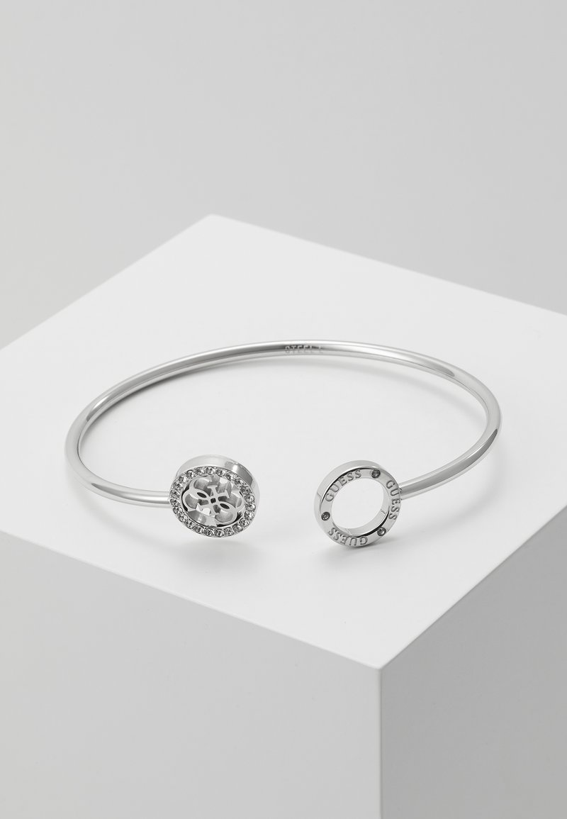 Bracelet jonc ouvert en argent avec une extrémité présentant un charm logo serti de pierres précieuses et l'autre un charm circulaire gravé.