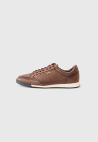 Baskets en cuir marron avec bout rond, fermeture à lacets, couture discrète et semelle blanche texturée. Minimalisme de la marque sur le côté.
